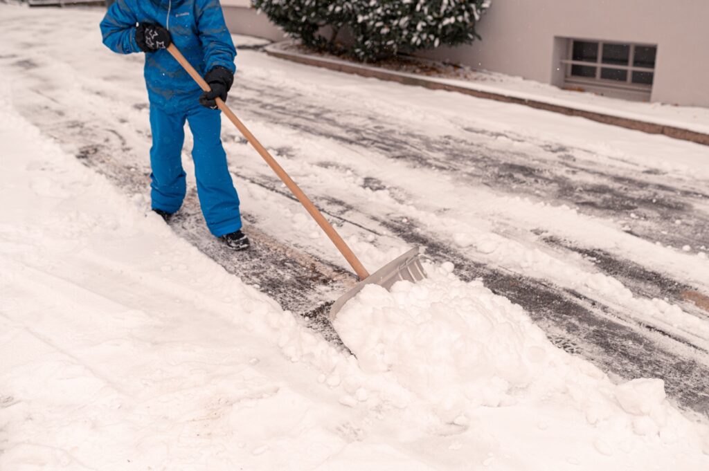 A schoolboy cleans snow from the footpath with a shovel